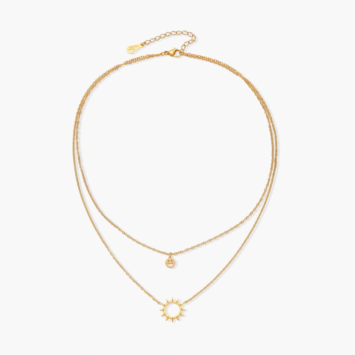 Gold layered necklace set with sunburst and smiley face pendants on delicate chains against white background.
