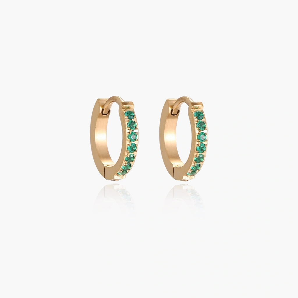 Pair of small gold huggie hoop earrings with bright green cubic zirconia stones on cream background